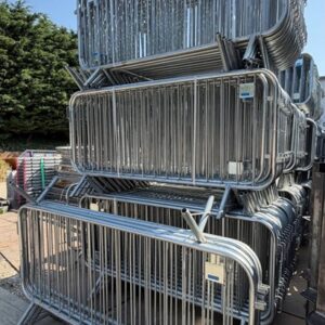 Heavy-duty galvanised steel crowd control barriers stacked outdoors for use at public events, roadworks and construction sites.
