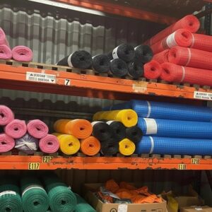 Rolls of scaffold debris netting in 50 metre lengths, available in various colours including pink, black, red, blue, yellow, orange, green and purple, stacked on warehouse shelving