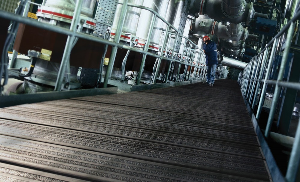 Industrial worker on ribbed plastic scaffold board walkway surrounded by pipes and equipment in processing facility