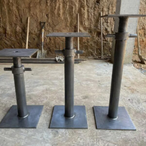 Three sizes of heavy-duty underpinning jacks (Size 1, Size 2, Size 3) with adjustable threaded shafts, large 200mm square base plates, and tommy bar handles, displayed together on a construction excavation site for foundation stabilizsation and subsidence repair