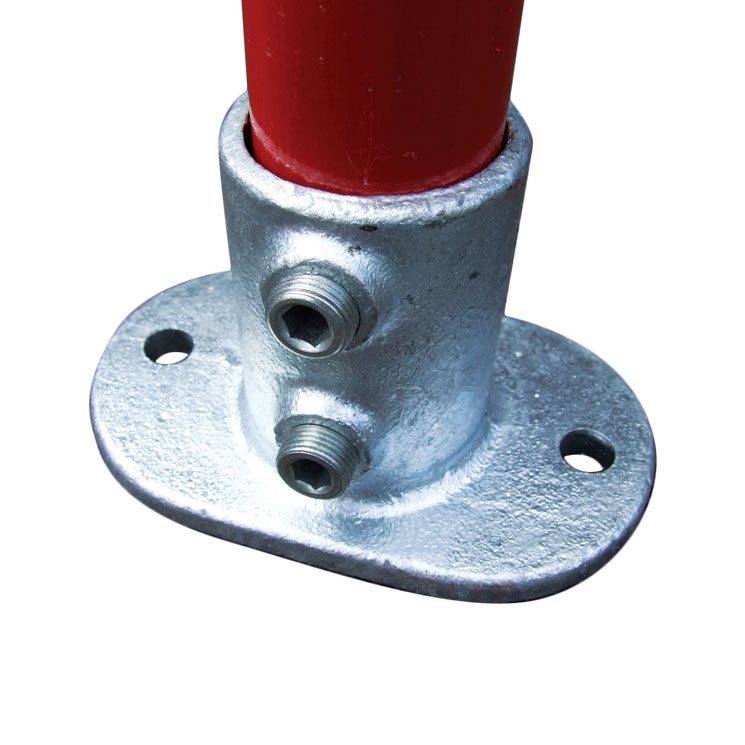 Close-up view of a galvanised Q Clamp Base Plate 132-4 fitting securely holding a vertical red-painted tube. The sturdy malleable iron clamp features a cylindrical spigot socket with two grub screw holes for tightening, mounted on an oval or elliptical base plate with two pre-drilled 14mm fixing holes for bolting to the ground or floor. The silver-grey hot-dip galvanised finish provides corrosion resistance, shown against a plain white background to highlight the product's robust construction and details.